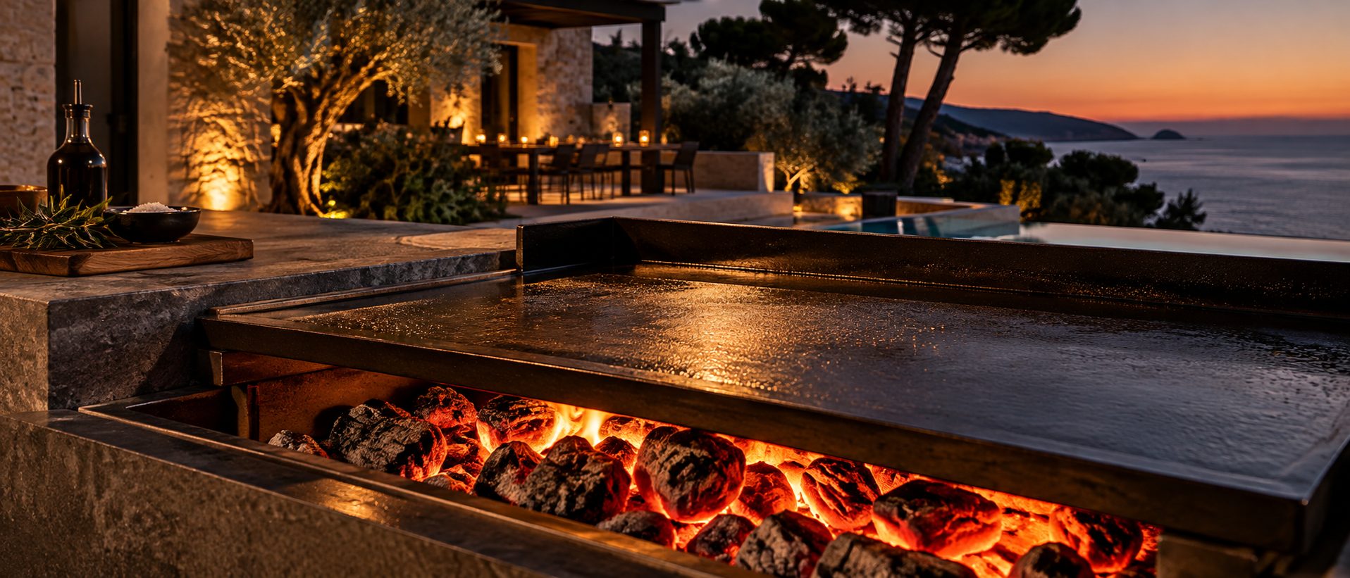 Plancha en acier sur un lit de braises, terrasse de villa face à la mer au crépuscule